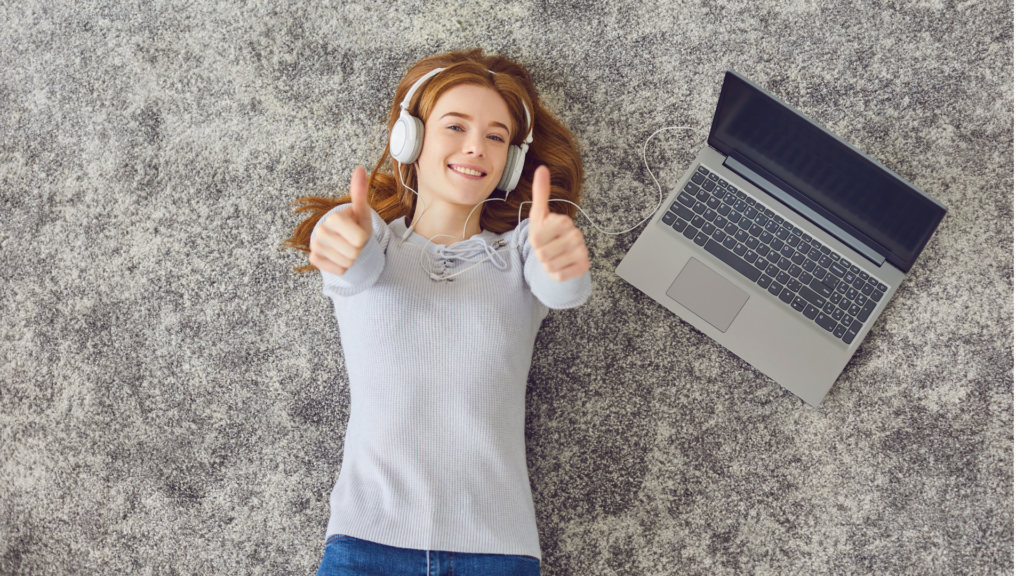 ヘッドホンをつけ両手で親指を立てる笑顔の女性とノートPC