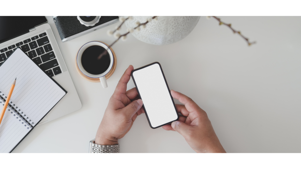 ノートPCやコーヒーが並ぶデスクでスマホを持つ手元